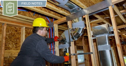 A technician installing ductwork during the HVAC rough-in phase of the home building process.